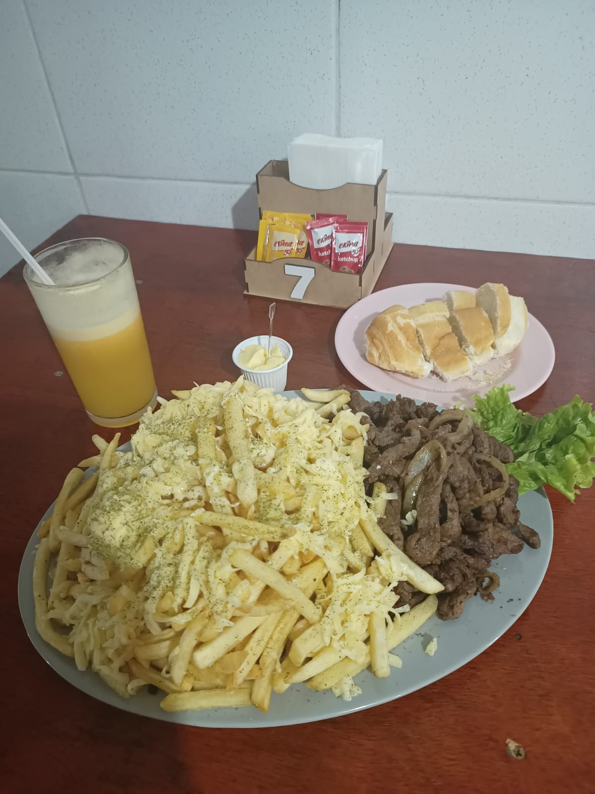 Porção de fritas com queijo, carne, pão e suco na mesa